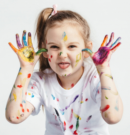 Little girl covered in paint making funny faces. Kindergarten kid. Prankster.